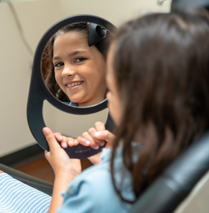 Young girl looking at smile in mirror during children's dentistry visit