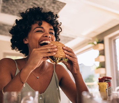 Woman smiling while eating sandwich in restaurant