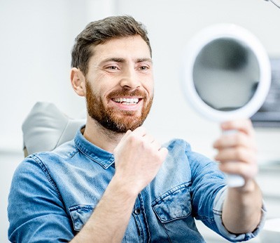 Man smiling at reflection in handheld mirror